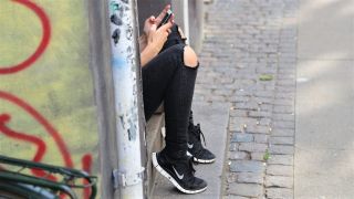 Person sitzt wartend an einem Hauseingang mit dem Handy in der Hand